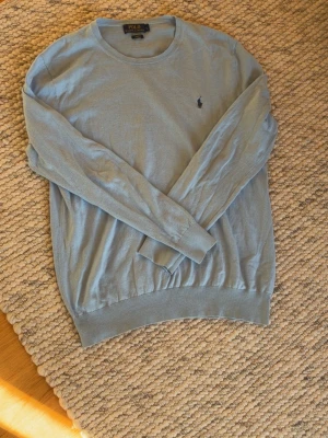 Ljusblå  tröja Polo Ralph Lauren - Snygg ljusblå stickad tröja från Polo Ralph Lauren i slim fit-modell. Tröjan har rund halsringning, långa ärmar och den klassiska broderade loggan på bröstet. Perfekt för dig som gillar stilrena och tidlösa plagg. Storlek L passar L-M