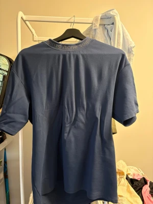Blå t-shirt från Acne Studios - Snygg blå t-shirt från Acne Studios med diskret logga i kragen. Klassisk passform och korta ärmar, perfekt till jeans eller shorts. Tillverkad i mjuk bomull för en skön känsla hela dagen.