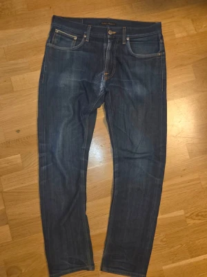 Mörkblå jeans från Nudie Jeans - Ett riktigt par feta Selvadge Nudie Jeans Modell Lean Dean  Dry Selvage Comfort  Storlek 33/34  Tvättade 3 ggr  Väldigt fint skick, med lagning i skrevet gjort av nudie jeans själva.  Ställ gärna och kom med prisförslag!