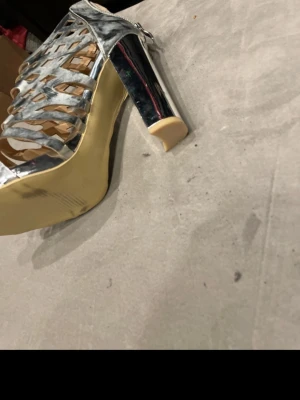 Silvriga pumps med klack och cut-outs - Unika pumps i metallic silver med hög blockklack och coola cut-out detaljer. Skorna har öppen tå och dragkedja bak för enkel påtagning. Materialet ser ut att vara konstläder med glansig finish. Perfekta för dig som vill sticka ut.