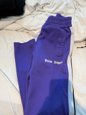 Lila mjukisbyxor Palm Angels - Säljer ett par lila mjukisbyxor från Palm Angels med vita sidoränder och elastisk midja. Byxorna har fickor och loggan tryckt i vitt på ena benet. Perfekta för en chill och trendig look. Kommit till användning två gånger så byxorna är i väldigt fint skick. 