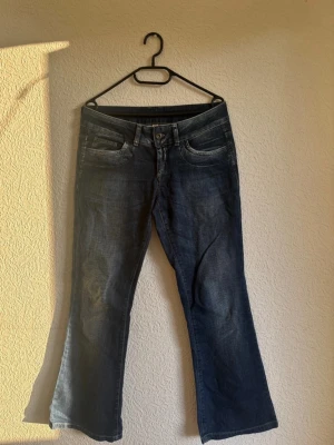 Mörkblå bootcut jeans - Säljer ett par mörkblå bootcut jeans med klassisk femficksdesign och snygga slitningar framtill. Jeansen har låg midja och lätt utsvängda ben, perfekta för en avslappnad och trendig look. Materialet är mjukt denim som sitter skönt hela dagen. Storlek nämns inte men skulle säga att de är storlek M. Fråga gärna om mått❣️