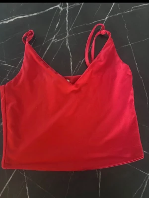Röd croppad linnetopp - Snygg röd croppad linnetopp med smala axelband och v-ringad hals. Perfekt till sommaren och enkel att matcha med jeans eller kjol. Materialet känns mjukt och stretchigt, vilket gör den bekväm att bära hela dagen.
