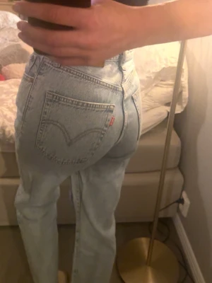 Levi's ljusblå 501 - Säljer ett par klassiska ljusblå Levi's jeans med rak passform och hög midja. Jeansen har fem fickor, ikoniska bakfickor med V-söm och en liten röd Levi's-tag. Tillverkade i slitstark denim, perfekta för en avslappnad och trendig look.