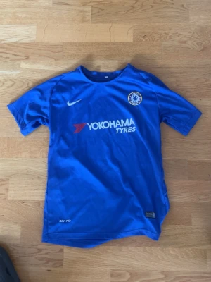 Chelsea FC matchtröja Nike blå - Chelsea FC matchtröja i blått från Nike med klubbmärke på bröstet och Yokohama Tyres som sponsortryck. Tillverkad i lätt och ventilerande material, perfekt för fotbollsträning eller match. Klassisk rund hals och korta ärmar.
