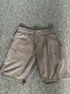Grå sweatshorts från FSBN - Mysiga grå sweatshorts från FSBN med dragsko i midjan och två sidofickor. Perfekta för chill dagar eller när du vill ha det bekvämt. Tillverkade i mjuk bomullsmix och har en relaxed fit.