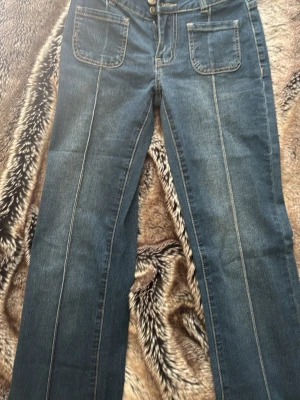 Blå jeans från madlad HELT NYA!  - Helt nya !! Säljer ett par blå jeans med lätt utsvängda ben och tydliga sömmar framtill. Jeansen har stora fyrkantiga fickor fram och dubbla knappar i midjan. Klassisk denimlook som passar till det mesta. Materialet är denim med kontrastsömmar. Regular längd. 