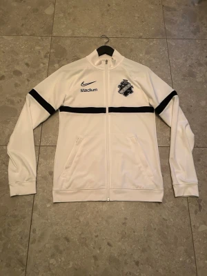 Vit Nike AIK träningsjacka - Säljer en vit träningsjacka från Nike med AIK-logga på bröstet och svarta detaljer. Storlek S passar nog även M. Skriv gärna vid funderingar.