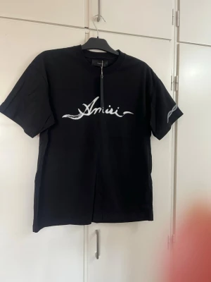 Svart Amiri t-shirt med tryck - Svart t-shirt från Amiri med vit logga och ormliknande tryck framtill och på ena ärmen. Klassisk rund hals och avslappnad passform. Perfekt för dig som gillar streetwear och vill sticka ut med en snygg detalj. Gjord i mjuk bomull.