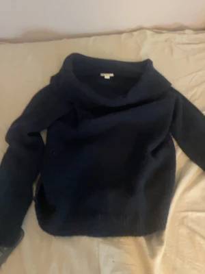 Mörkblå stickad tröja med polokrage - Mysig mörkblå stickad tröja med bred polokrage och långa ärmar. Perfekt för kyliga dagar och enkel att matcha med jeans eller kjol. Tröjan har en avslappnad passform och är stickad i ett mjukt material.