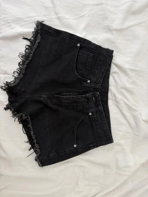 Svarta jeansshorts med fransad kant - Svarta denimshorts med fransad kant och klassisk femficksdesign. Shortsen har en hög midja och råa benslut för en avslappnad look. Perfekta för sommaren och enkla att matcha med olika toppar.