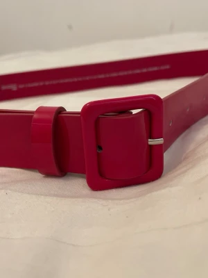 Rött bälte med fyrkantigt spänne - Snyggt rött bälte med ett matchande fyrkantigt spänne i plast. Bältet har en stilren design och är perfekt för att ge outfiten en färgklick. Justerbar längd med flera hål för bästa passform.