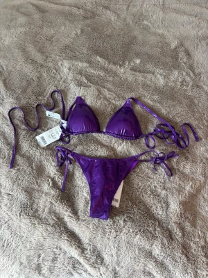 RESERVERAD!! Oanvänd lila bikini från Calzedonia - Snygg lila bikini set från Calzedonia. Båda delarna har knyt i sidorna och i ryggen för justerbar passform. Materialet har en glansig finish, perfekt för stranden eller poolen! Prislapp kvar!🙌🏼🤩