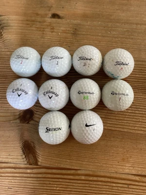 10 vita golfbollar från olika märken - Säljer ett set med 10 vita golfbollar från kända märken som Titleist, Callaway, TaylorMade, Srixon och Nike. Bollarna är runda med dimple-mönster och tillverkade i syntetmaterial. Perfekt för golfträning eller spel på banan.