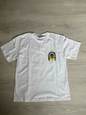Vit t-shirt från Casablanca - Säljer en vit t-shirt från Casablanca med ett färgglatt tryck på bröstet som föreställer en byggnad och texten 'Avenida Casablanca'. T-shirten har rund hals och korta ärmar. Perfekt för dig som gillar stilrena plagg med unika detaljer.