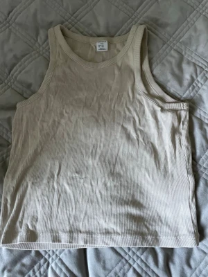 Beige ribbad linnetopp från Lindex - Snygg beige ribbad linnetopp från Lindex. Toppen är ärmlös och har en klassisk rund halsringning. Perfekt att matcha med jeans eller kjol för en enkel och stilren look.  Modern och luftig perfekt sommar plagg!
