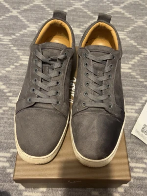 Grå vita Loubitin - Snygga grå sneakers i mocka med klassisk låg profil och vita sulor. Skorna har matchande grå skosnören och en mjuk, beige insida. Perfekta för dig som gillar stilrena och minimalistiska sneakers. Använd enstaka gånger.