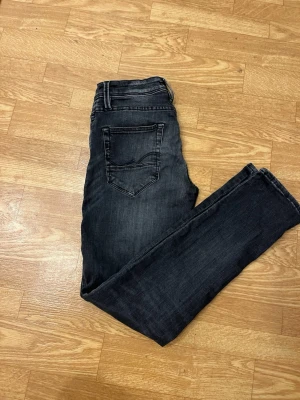 Svarta slim fit jeans Jack & Jones - Snygga svarta slim fit jeans från Jack & Jones med klassisk femficksdesign och diskreta slitningar. Jeansen har en smal passform och är tillverkade i stretchigt denim för extra komfort. Perfekta för en trendig och avslappnad look. Storlek w30-l32