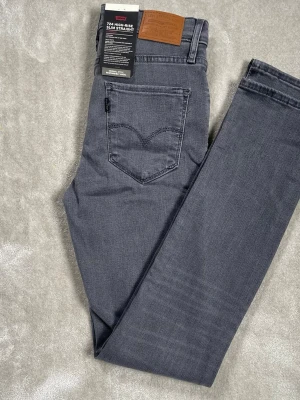 Grå Levi's 724 High-Rise Slim Straight - Snygga grå jeans från Levi's modell 724 High-Rise Slim Straight. Jeansen har hög midja, raka ben och klassiska fem fickor. Tillverkade i mjukt denimtyg med stretch för extra komfort. Perfekta för en trendig och avslappnad look.