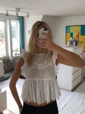 Vit topp/blus  - Söt vit blus med volangärmar och broderade spetsdetaljer. Toppen har en luftig passform, rund halsringning och vackert hålmönster nertill. Perfekt för sommaren och ger en romantisk vibe till din outfit.