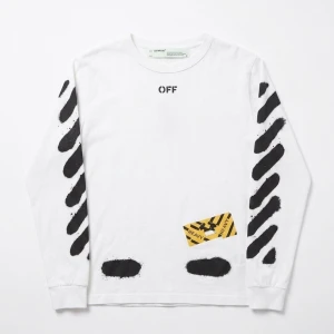 Vit långärmad Off-White t-shirt - Säljer en vit långärmad t-shirt från Off-White med svarta diagonala ränder på ärmarna och stor text på ryggen. Framsidan har tryck med OFF och en gul detalj. Tillverkad i mjuk bomull och har en avslappnad passform.