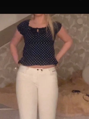 Mörkblå prickig blus med volang - Supersöt mörkblå blus med vita prickar och volangdetaljer vid ärmslut och nederkant. Blusen har korta puffärmar och en liten öppning med knyt framtill.🥰 Det är storlek 40 men passar mig som bär 36