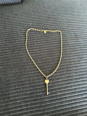 silver halsband med nyckelberlock - Snyggt halsband i silver metall med en kedja och en berlock formad som en nyckel med hjärtdetalj. Perfekt accessoar för dig som gillar unika smycken med lite vintagekänsla. Passar till många olika stilar och är lätt att matcha.