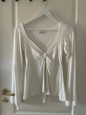 Design by si tröja  - Supersnygg vit långärmad topp från design by si med djup v-ringning och knyt framtill. Tunt och mjukt material som sitter skönt på kroppen. Perfekt att styla med jeans eller kjol för en trendig look. Storlek xs/s, använd en gång 