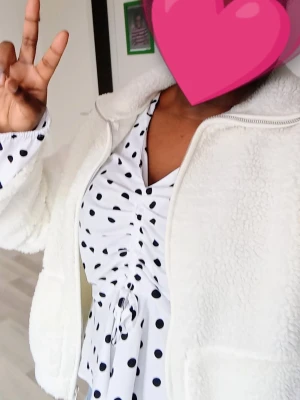 Prickig blus med rynk framtill - Vit blus från Boohoo med svarta prickar, djup V-ringning och rynkdetalj med knyt framtill. Långärmad modell i lätt och luftig kvalitet, perfekt för en trendig look. Snygg passform som framhäver midjan.