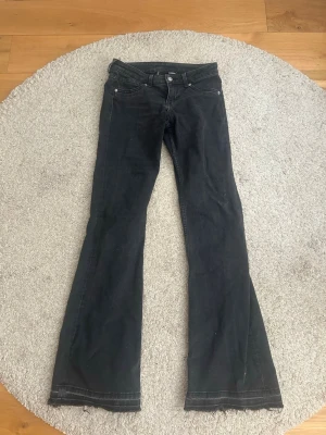 Svarta bootcut jeans - Snygga svarta bootcut jeans med klassisk femficksdesign och låg midja. Jeansen har utsvängda ben och stängs med knapp och dragkedja. Perfekta för en trendig och avslappnad look.
