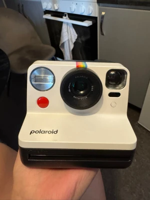 Polaroid Now vit instantkamera - Säljer en Polaroid Now instantkamera i vit plast med svart bas. Använd 2-3 gånger, i nyskick i original förpackning, utan laddare (kan laddas med usb-c sladd) Kameran har en klassisk retrodesign, stor röd avtryckare, inbyggd blixt och regnbågsdetalj ovanför linsen. Perfekt för att ta analoga bilder direkt och få dem utskrivna på plats, säljs med 2 paket med film/bilder. 8 st stora bilder i varje paket.  Kan säljas utan film/bilder för 1200kr