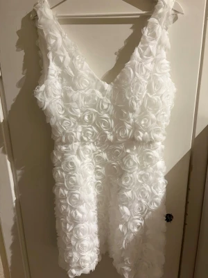 Vit kort klänning med 3D-blommor - Superfin vit kort klänning med 3D-blommor över hela tyget och v-ringad hals. Passar jättebra till studenten och sommaren.