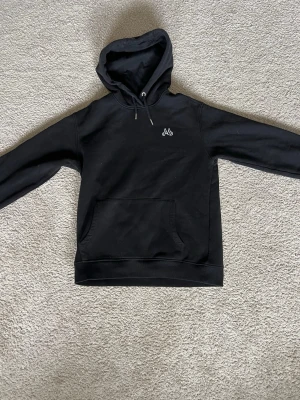 Svart hoodie från maggiore  - Svart hoodie från Maggiore med vit broderad logga på bröstet. Klassisk modell med huva och dragsnören samt stor magficka framtill. Tillverkad i mjukt material som passar perfekt till en avslappnad stil.