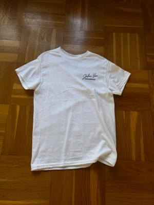 Vit t-shirt från Julian Vane - Vit t-shirt från Julian Vane med diskret logga broderad på bröstet. Klassisk rund hals och korta ärmar, perfekt för en clean och enkel look. Materialet är mjuk bomull som känns skönt mot huden. Snyggt minimalistisk design med Stockholm-tryck.