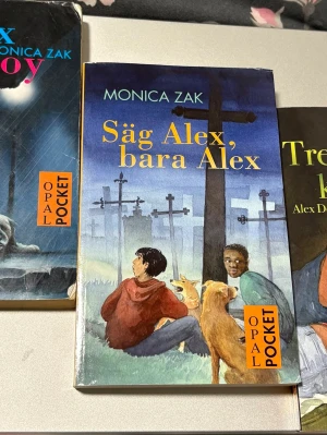 Säljer 3 böcker ur den populära dogboy serien  - En pocketbok av Monica Zak med titeln 'Säg Alex, bara Alex'. Omslaget har en illustration av två ungdomar och en hund som sitter på gräs vid ett järnvägsspår, med blå och gröna färgtoner. Boken är utgiven av Opal och har ett mjukt omslag.