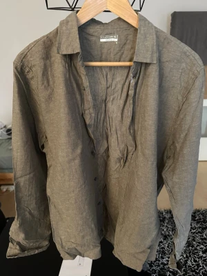 Olive linneskjorta från Intimissimi - Snygg olive skjorta i linne från Intimissimi. Skjortan har klassisk krage, knappar framtill och långa ärmar. Perfekt för en avslappnad och stilren look.