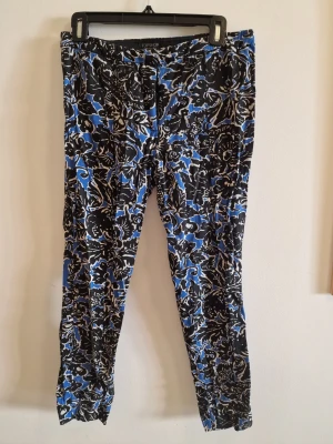 Mönstrade byxor från Topshop - Säljer ett par unika byxor från Topshop i storlek 38. Byxorna har ett coolt blommigt mönster i svart, blått och vitt. De är smala i modellen och har resår i midjan för extra komfort. Perfekta för dig som vill sticka ut med din stil!