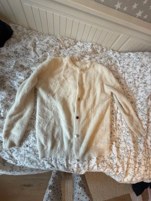 Unik Fluffig kofta med olika knappar - Denna jätteunika långa krämfärgade kofta med olika knappar är perfekt för dig som vill ha en cool, unik och vintage look.  Passar strl xxs-s/m och för  flickor som är 150-170cm?  Lite tråddragningar men inget som märks då den är fluffig och lite smutsig i ärmslut. Supermjuk och fluffig kofta i krämvit färg med rund halsringning och långa ärmar. Koftan har dekorativa pärlemorknappar framtill, varav en är i en annan färg för en unik touch. 