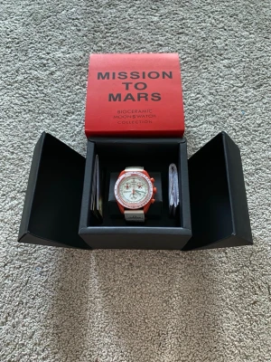 Omega x Swatch Mission to Mars klocka - Säljer en Omega x Swatch Mission to Mars från Bioceramic MoonSwatch Collection. Klockan har en vit urtavla med röda detaljer och röd boett, samt vitt armband med Omega-logga. Snygg och unik design som sticker ut på handleden.