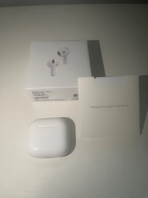 Apple AirPods gen 4 - Säljer ett par vita Apple AirPods med tillhörande laddningsetui. Snygg och stilren design i blank plast, perfekt för dig som vill ha trådlösa hörlurar till mobilen. Kommer med originalförpackning och dokumentation.