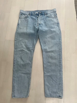 Ljusblå raka jeans i klassisk modell - Säljer ett par ljusblå jeans med rak passform och hög midja. Storlek 31 30. Jeansen har fem fickor, knappgylf och klassisk denimlook. Perfekta för en avslappnad och trendig stil.