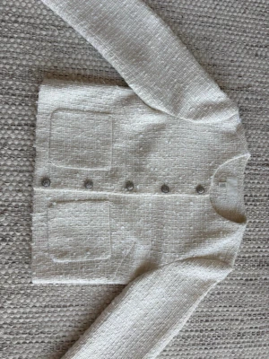 Vit tweedkofta med fickor från H&M  - Vit tweedkofta i storlek XS. Koftan har två fickor och silverknappar som går att knäppa upp. Tyget glimmrar i solen som ger en silver effekt. 
