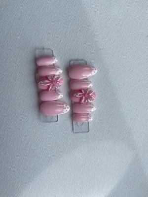 Rosa press-on naglar med blommor - Säljer ett set press-on naglar i ljusrosa med vita franska tippar och rosa prickar. Två naglar har 3D-blommor i rosa och vitt för extra detalj. Ovala och korta till medellånga, perfekta för en söt och trendig look. 