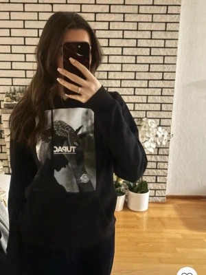 Svart Tupac hoodie med tryck - Säljer en svart hoodie med stor Tupac-print på bröstet. Hoodien har huva med dragsko och en klassisk magficka framtill. Materialet känns mjukt och bekvämt.