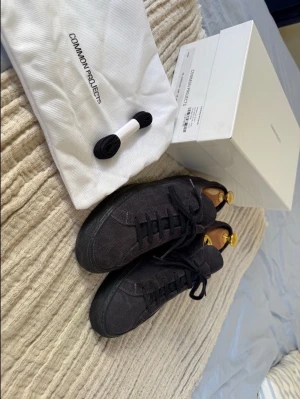 Svarta mockasneakers från Common Projects Storlek 41 - Stilrena premiumsneakers från Common Projects, Achilles Low Suede Navy. Mörkblå mocka. Mycket bra skick, väldigt lite använda. Originalkartong, dustbag och extra skosnören (original) ingår. Skoblock ingår ej.  Nypris omkring 4000 kr. Pris kan diskuteras, hör av dig 