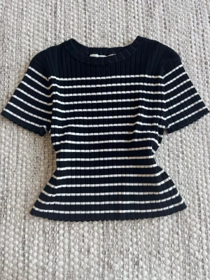 Svartvit ribbad randig topp - Snygg ribbad topp med svart och vitt randigt mönster. Modellen är figurnära och har ett mjukt och stretchigt tyg. 