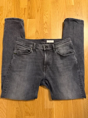 Grå slim fit jeans från Tiger of Sweden 30/32 pistolero - Snygga grå slim fit jeans från Tiger of Sweden med klassisk femficksdesign och diskret tvättad look. Jeansen har raka ben och är tillverkade i mjukt denim-material som ger en skön passform. Perfekta för dig som gillar stilrena och moderna jeans.