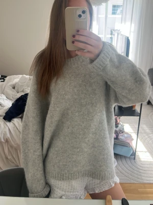 Ljusgrå oversized stickad tröja - Mysig ljusgrå stickad tröja med oversized passform och rund hals. Tröjan har långa ärmar och ribbade muddar vid ärmslut och nederkant. Perfekt för lager-på-lager och chill dagar.