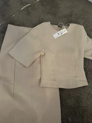 Beige bodyset från Zara - Snyggt beige set från Zara med kortärmad topp och matchande underdel. Setet har en minimalistisk design med raka linjer och mjukt material som känns skönt mot huden. Perfekt för dig som gillar stilrena och enkla plagg. Lappen sitter kvar.