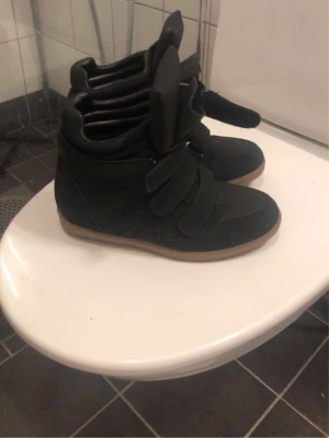 Svarta höga sneakers med kardborre - Snygga svarta sneakers med högt skaft och tre breda kardborreband. Skorna har en chunky gummisula i beige och är tillverkade i mockaliknande material. Perfekt för dig som gillar streetstyle och vill ha något unikt på fötterna. Har använt 1 till två gånger så inga skador 